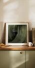 a framed photograph of a green leaf on a kitchen counter, with a coffee maker and other kitchen items visible in the background.