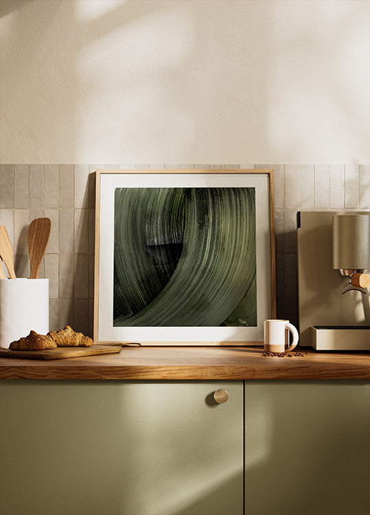 a framed photograph of a green leaf on a kitchen counter, with a coffee maker and other kitchen items visible in the background.