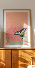 a framed painting of a butterfly on a pink flower, displayed on a wooden cabinet or shelf.