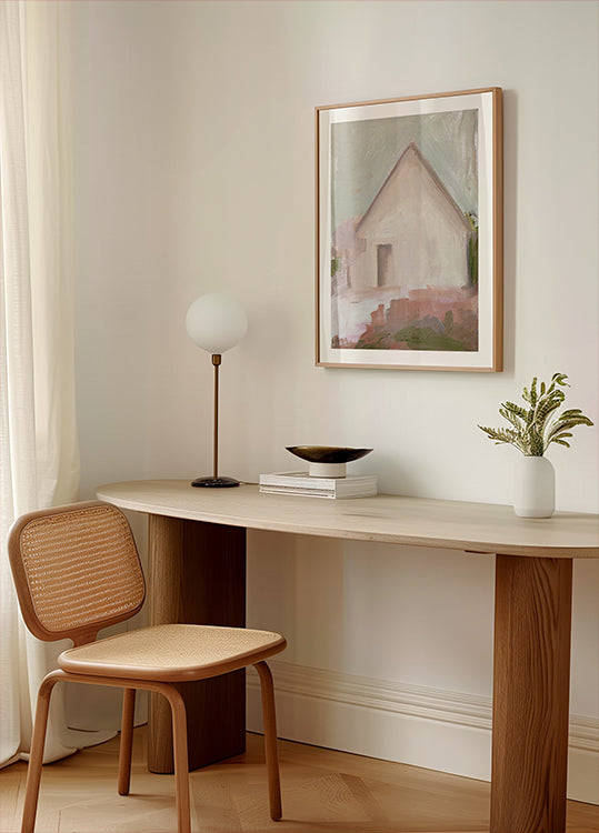a modern, minimalist workspace with a wooden desk, a woven chair, a lamp, and a framed painting of a house.