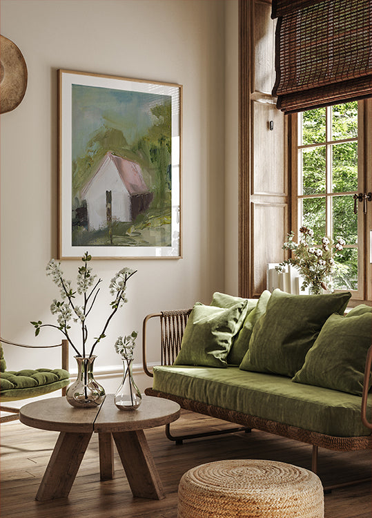 a cozy living room with a large window, a green sofa, a wooden coffee table, and a framed painting of a house.
